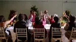 11 people around a dining table raising glasses. The table is adorned with flowers.