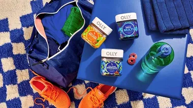 A flatlay image of OLLY vitamins and supplements. Nearby a water bottle and orange training shoes are pictured.