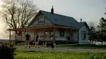 A man with a child on his shoulders, a woman, a small girl and a dog walk up to a farm house